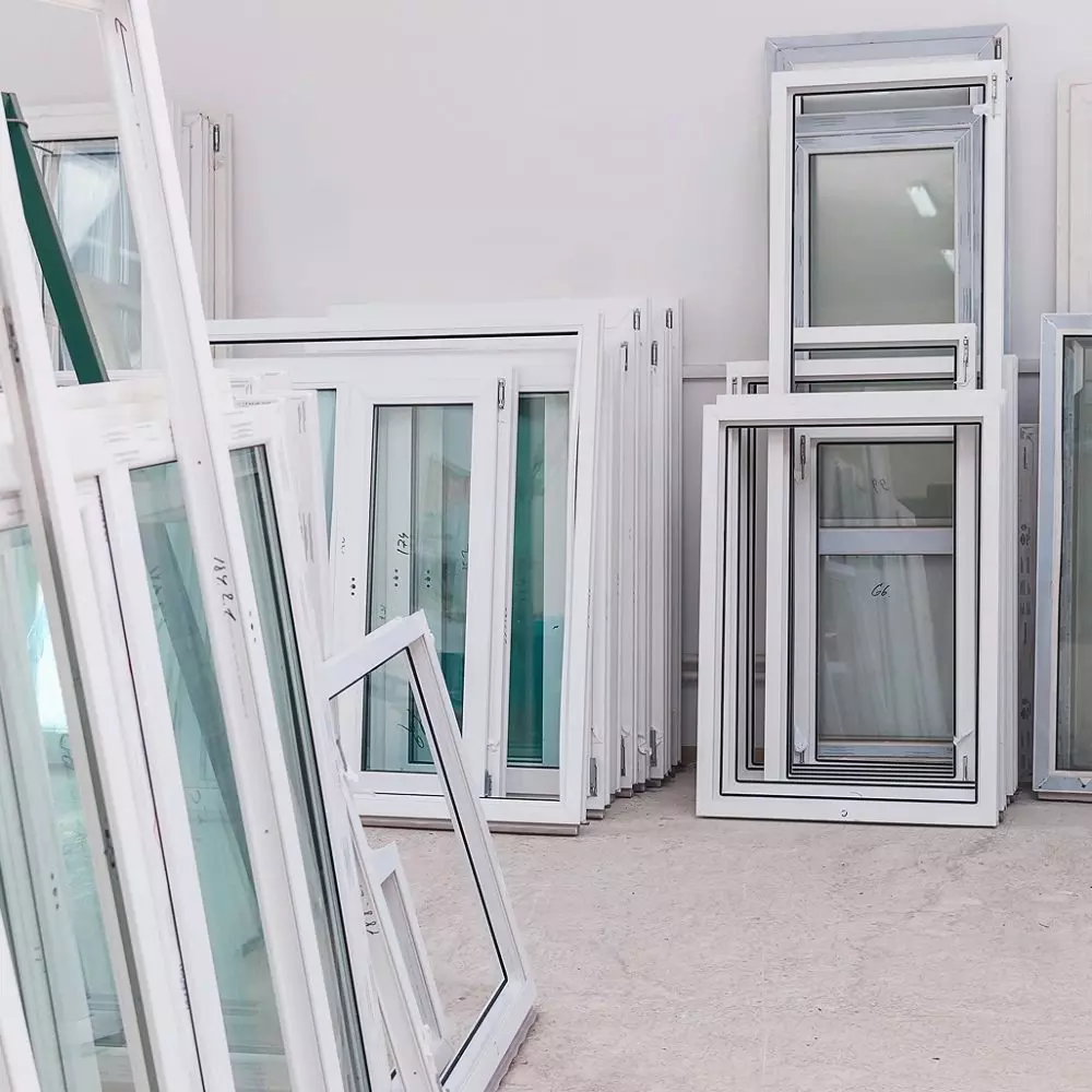 Finestre in alluminio allineati in magazzino, pronti per installazione, con cornici bianche su pavimento neutro.