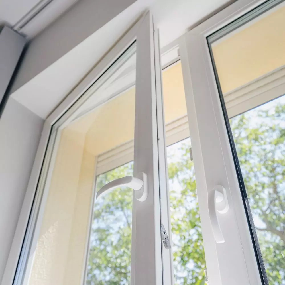 Finestra socchiusa in stile moderno con telaio bianco, luce naturale entering e vista su albero all'esterno.