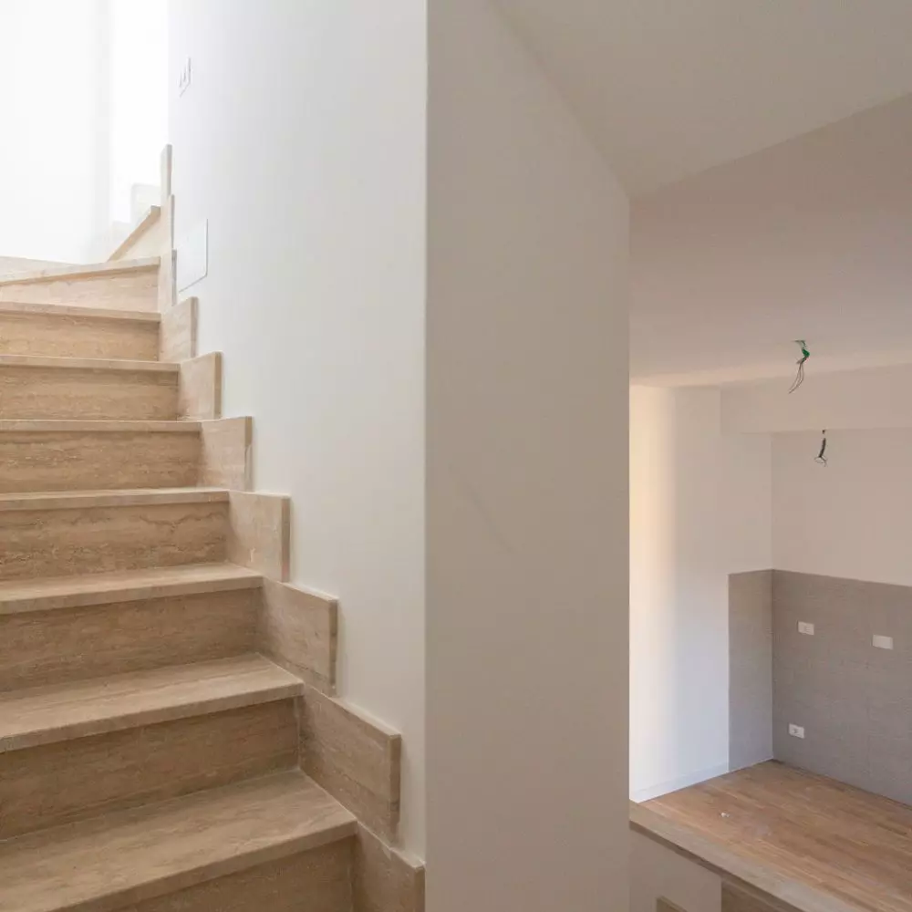Ristrutturazione Casa: scalinata in legno in stile moderno, con pareti bianche illuminate, interno di casa in costruzione.