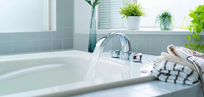 Sostituzione vasca con doccia: rubinetto che eroga acqua nella vasca, con piastrelle azzurre, piante in vasi e asciugamani piegati sul bordo.